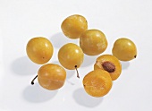 Whole and halved yellow mirabelle plums on white background