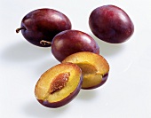 Whole and halved plums on white background