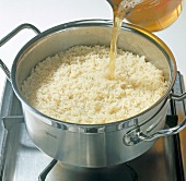 Close-up of vegetable broth being poured in boiled long grain rice in casserole