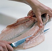 Close-up of hand cutting lower head of fish, step 8