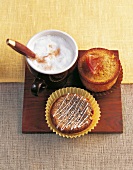 Muffins, Mohn-Muffin und Orangen -Muffin + Cappuccino auf Brettchen