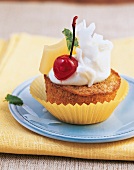 A pina colada muffin decorated with coconut and a cherry on a plate