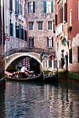 Tourists enjoying gondola ride in narrow canal, Venice, Italy