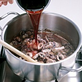 Close-up of red wine being poured on squid and vegetable mixture in casserole, step 3