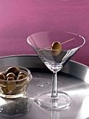 Cocktail glass with skewered olive on tray