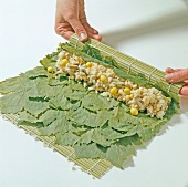 Close-up of hand rolling mat stuffed with rice on grape leaves, step 1