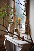 Lit candle and stone vase with rose hip in front of mirror