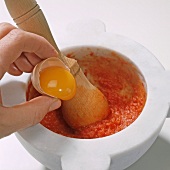 Close-up of egg yolks being added in mortar with mixture, step 4