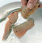 Close-up of hand putting roach fish fillets in flour, step 1