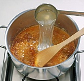 Fish stock being poured in pot with mixture of onion, step 4