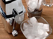 Close-up of ice crusher, jar and bowl of ice cubes on wooden table