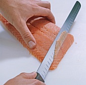 Close-up of hand cutting thin slices of salmon