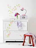 White chest of drawers with floral detail continuing onto white wall