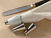 Close-up of icing bag, spatula and steel nozzles on beige background