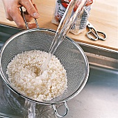 Sushi - Reis wird in einem Sieb unter fließendem Wasser gewaschen