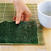 Sushi - Noriblatt wird auf eine Bambusrollmatte gelegt