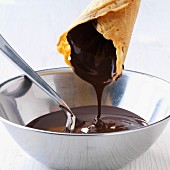 An ice cream cone being dipped into liquid chocolate