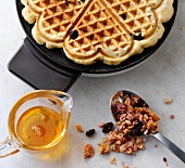 Cereal waffles in waffle iron and glass jug of maple syrup