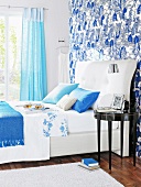 White double bed with patterned wallpaper and blue curtains in bedroom