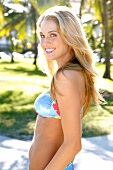 Portrait of beautiful blonde woman in colourful bikini standing on beach in Miami, smiling