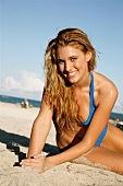 Portrait of blonde woman wearing blue bikini lying on beach, smiling
