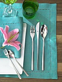 Silver cutlery and pink flower on green and white place setting
