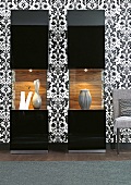 Illuminated display case with black and white patterned wallpaper and chair