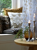 Lit candles and curtain in front of cushions on window sill