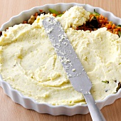 Mashed potatoes being spread for vegetable pie in ramekin, step 2