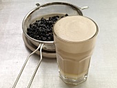 Glass of white espresso and espresso beans in colander