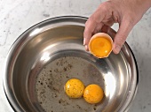 Close-up of hand pouring egg yolks in bowl for preparation of bearnaise sauce, step 1