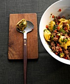 Thai tortellini salad in bowl beside spoon and wooden board