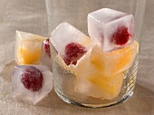 Ice cubes with fruit pieces in glass and some fallen outside