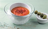Chilled cream of tomato in bowl beside green olive skewers