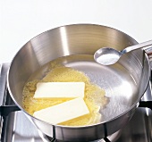 Butter being cooked in pan and salt being added for preparation of choux pastry, step 1