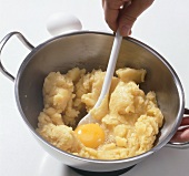 Close-up of egg being mixed with mass in casserole for choux pastry, step 5