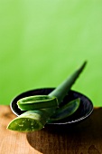 Close-up of bowl with aloe vera branch kept on wooden table against green background