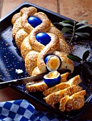 Osterzopf with blue eggs and sesame seeds in baking tray with knife