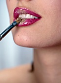 Close-up of woman's lips wearing red lipstick, applying golden dust on it with brush