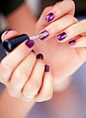 Close-up of woman applying gold dust on purple nail polish