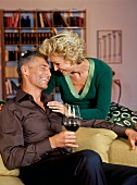 Happy mid-aged couple relaxing in living room with man having a glass of red wine, smiling