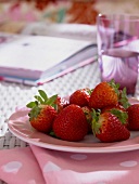 Erdbeeren auf einem Teller, Wassergl as und ein Buch auf einem Tisch