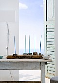 Blaue Kerzen in Kerzenständern auf einer Holzplanek vor offenem Fenster