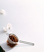 Cocoa powder in strainer with egg shells on white background