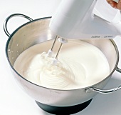Close-up of cream being beaten in pan with beater for preparation of chocolate, step 2