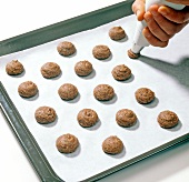 Close-up of hemisphere shaped chocolate being piped on baking tray with icing bag