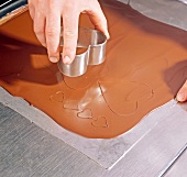 Sheet of couverture chocolate being cut with heart shaped mould