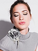 Beautiful woman wearing grey top with floral brooch and make-up, pouting with eyes closed