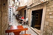 Gasse in Dubrovnik, Menschen sitzen an Tischen