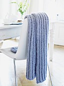 A blue knitted throw hanging over the back of a chair